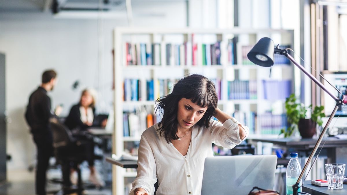 Software developer burnout concept image showing female programmer sitting at a desk looking stressed.