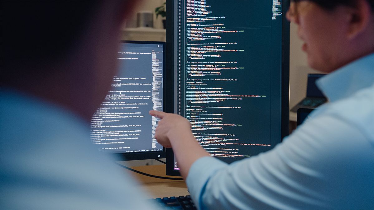 Python developers working at a computer station observing code on multiple split screen displays.